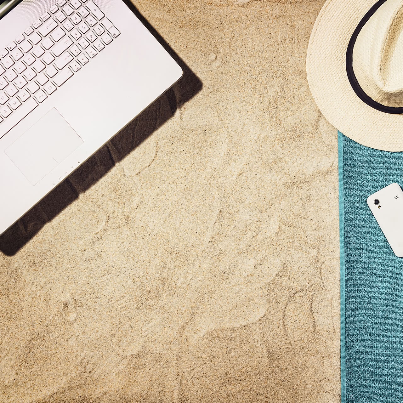 laptop on sand and summer hat on towel