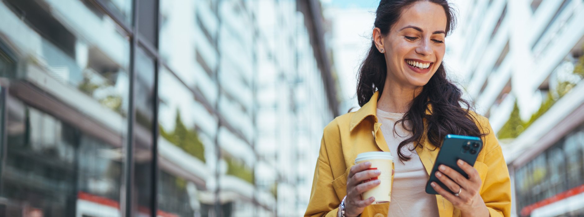 woman with coffee in her hand looking at her phone smiling