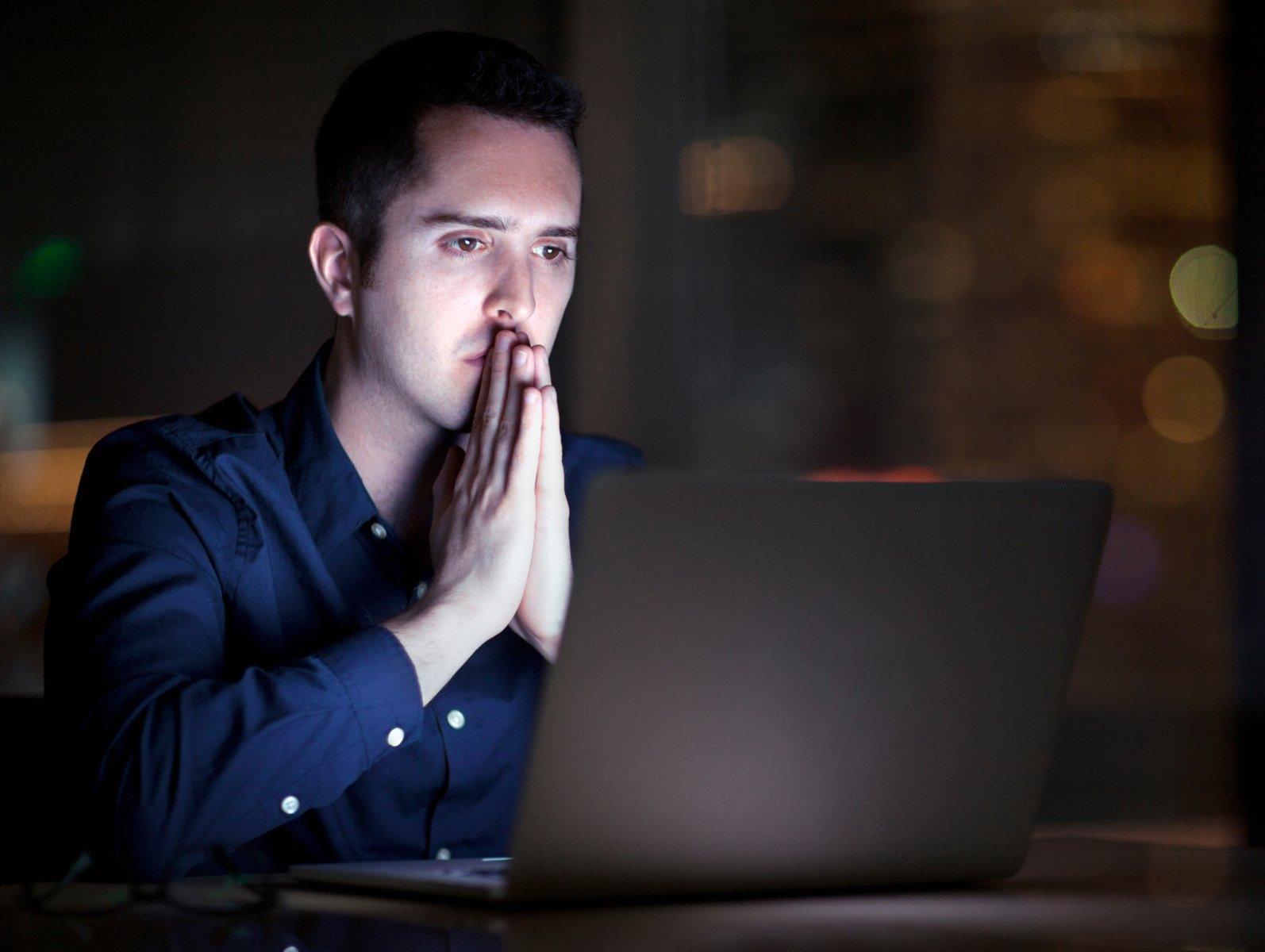 man in front of laptop with praying gesture