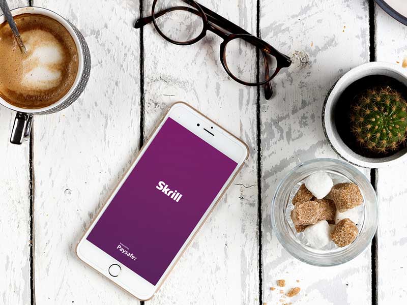 phone with open Skrill app on a white table with coffee cup and glasses