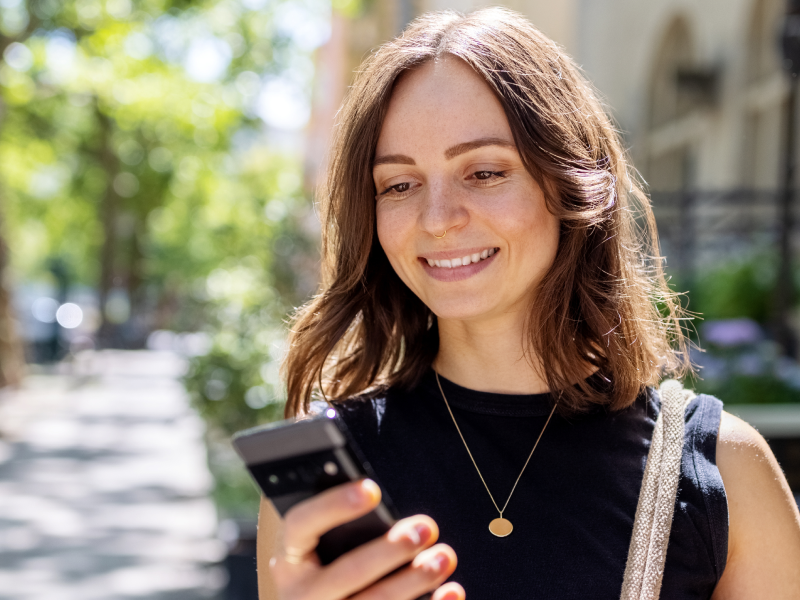 woman on the street smiling at her mobile phone