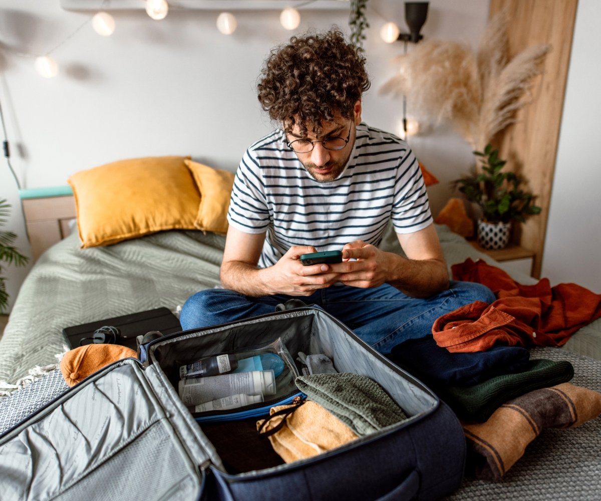man looking at his phone with a packed suitcase in front of him
